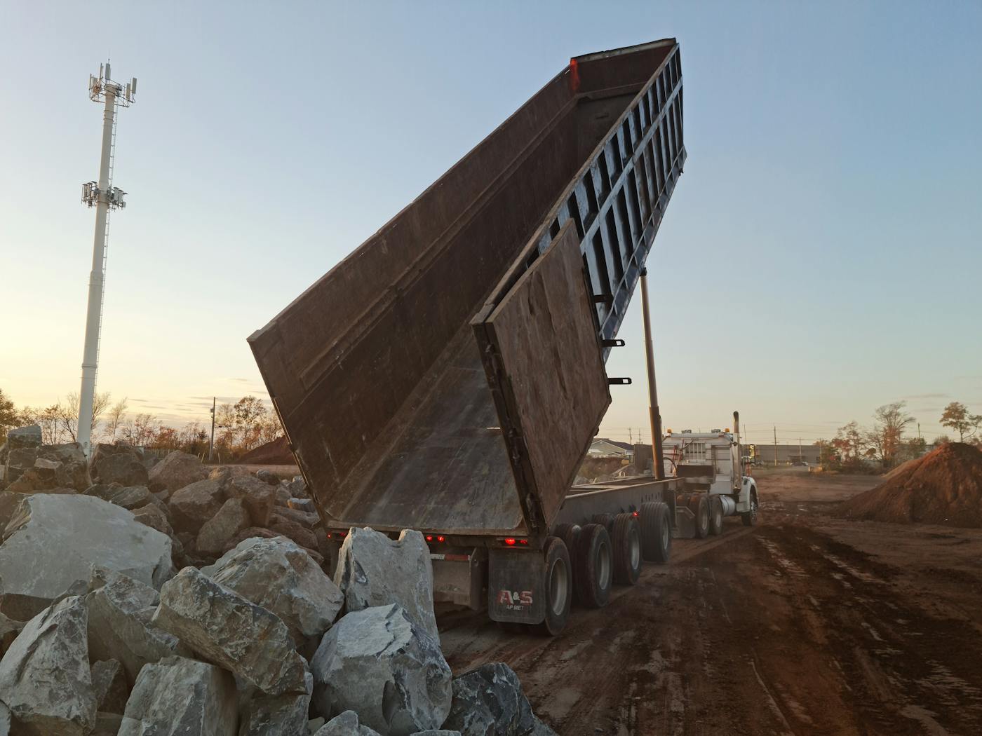 BT Trucking end dump truck unloading rocks at dusk